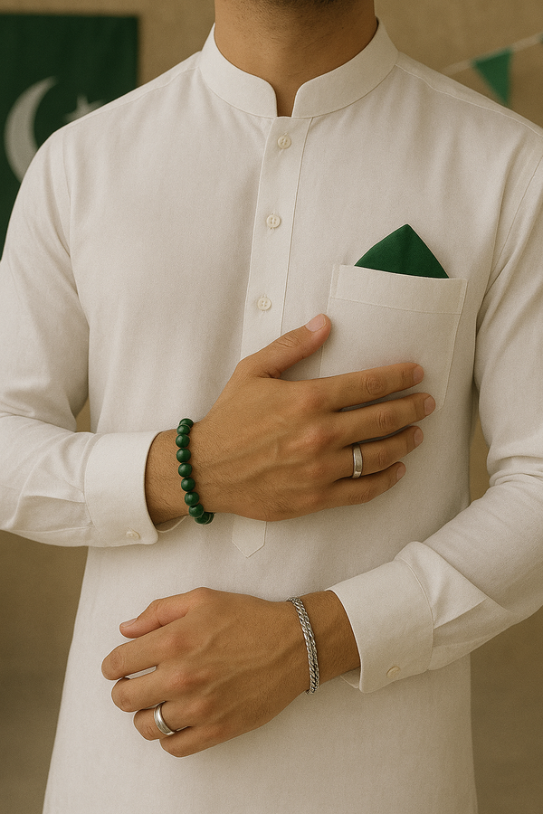Close-up of a man in a white shalwar kameez with a green pocket square, wearing silver rings, a green beaded bracelet, and a silver braided bracelet.