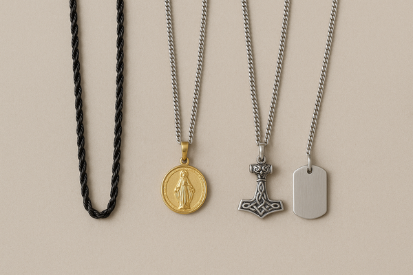 Four men’s necklaces on a beige background: a black rope chain, a silver chain with a gold medallion, a silver chain with a Viking hammer pendant, and a silver chain.