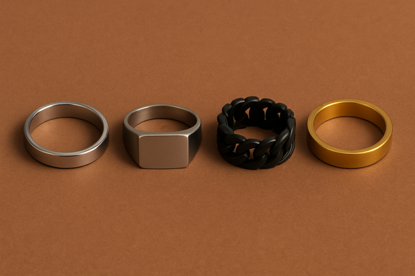 Four men’s rings on a brown background: silver minimalist band, silver signet, black Cuban-style, and gold matte ring.