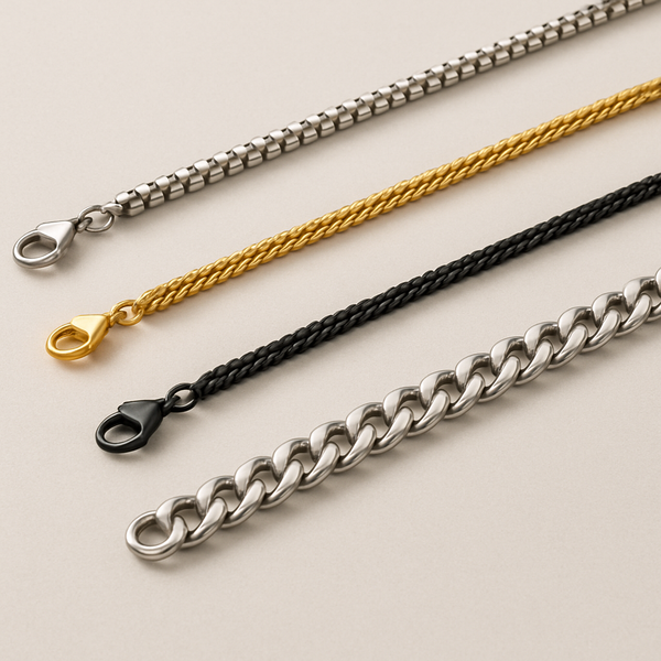 Close-up of four minimalist men’s chain necklaces laid out on a neutral background, featuring a silver box chain, gold rope chain, black rope chain, and silver Cuban chain, each with matching clasps.