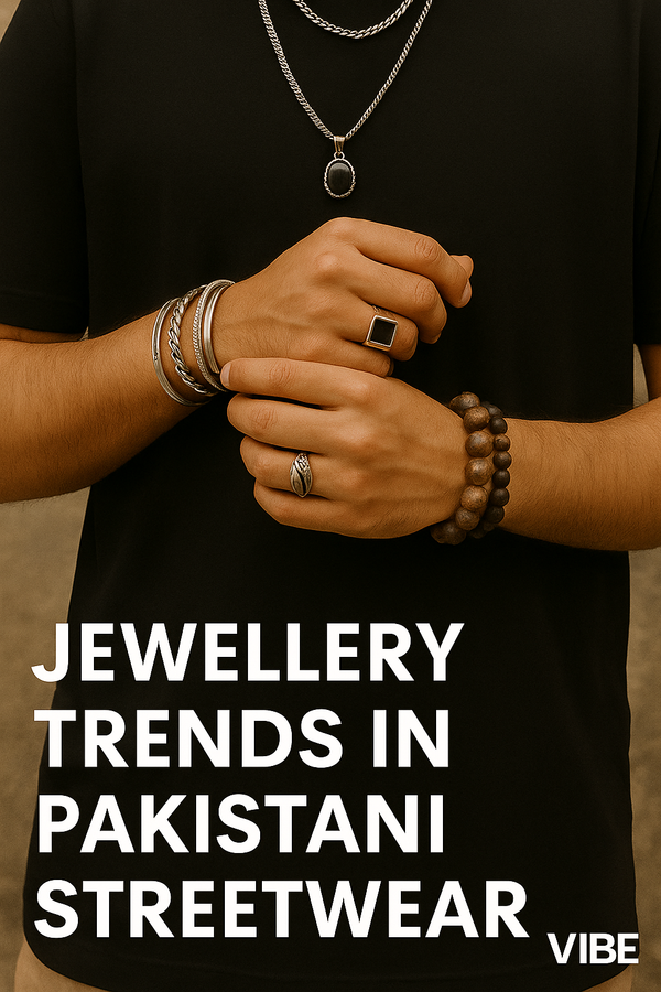 Cropped view of a man's hands wearing chunky rings, layered silver chains, beaded bracelets, and minimalist cuff bracelets, showcasing 2025 Pakistani streetwear jewelry trends by VIBE.