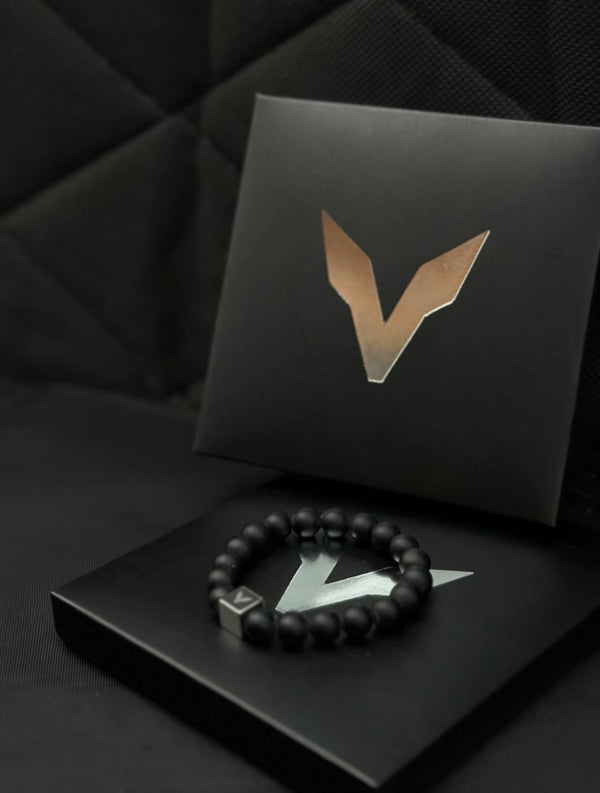 Black beaded bracelet on a black box with a logo, against a dark background
