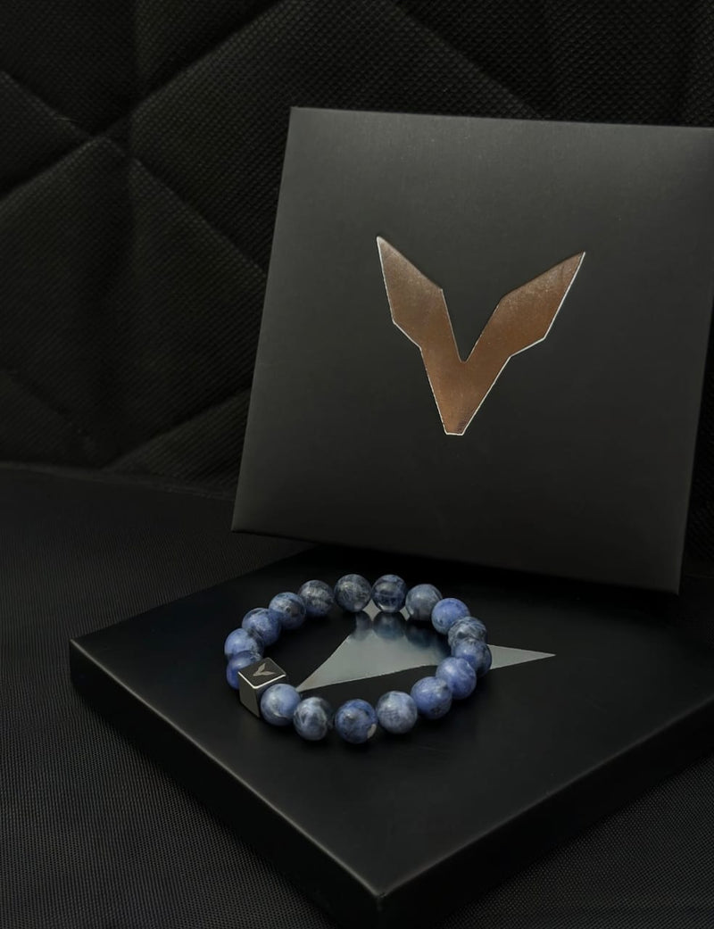 Blue beaded bracelet on a black box with a brand logo in the background