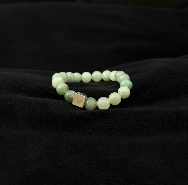 Green beaded bracelet with a square metal charm on a black fabric background