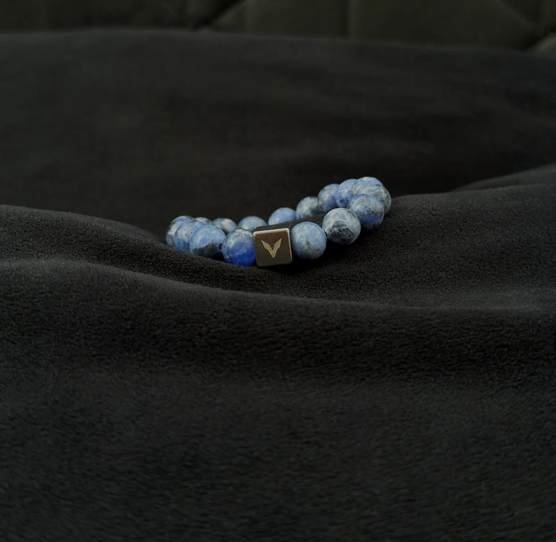 Blue beaded bracelet with a gold clasp on a black fabric background