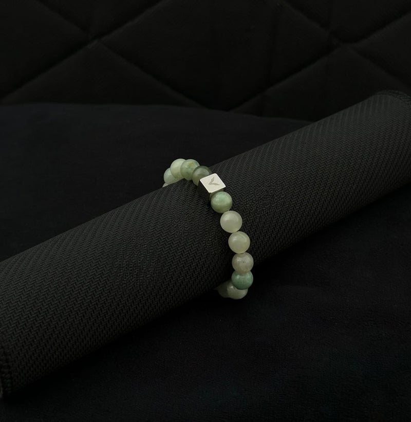 Green beaded bracelet with a silver clasp on a black textured surface