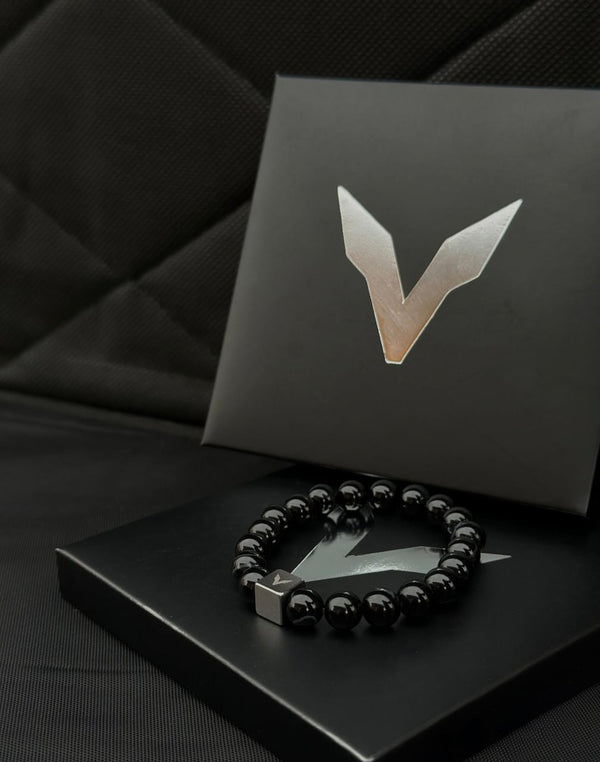 Black beaded bracelet on a black box with a logo, against a dark background