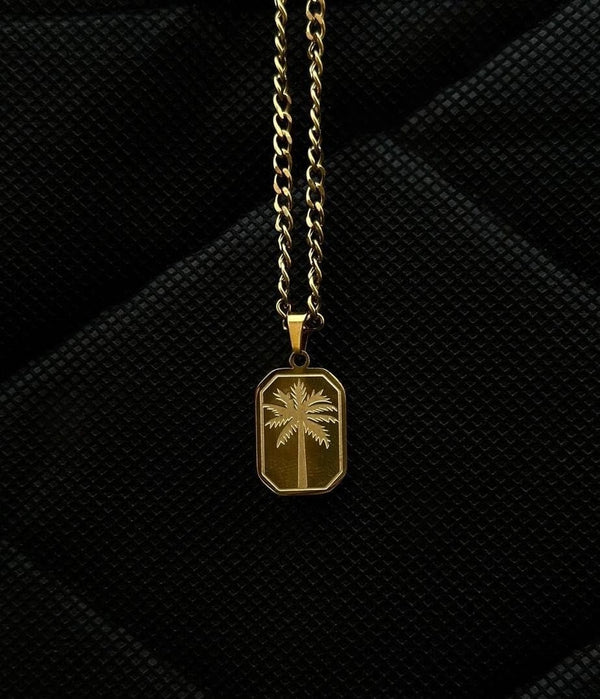 Gold necklace with a palm tree pendant on a black textured background