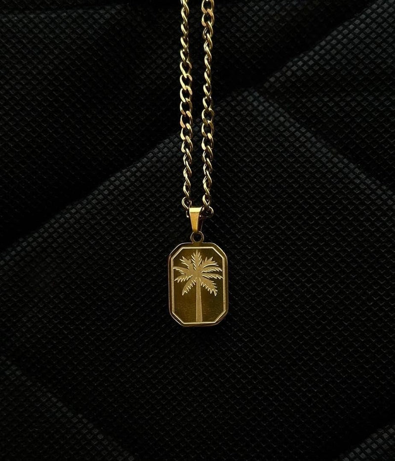 Gold necklace with a palm tree pendant on a black textured background